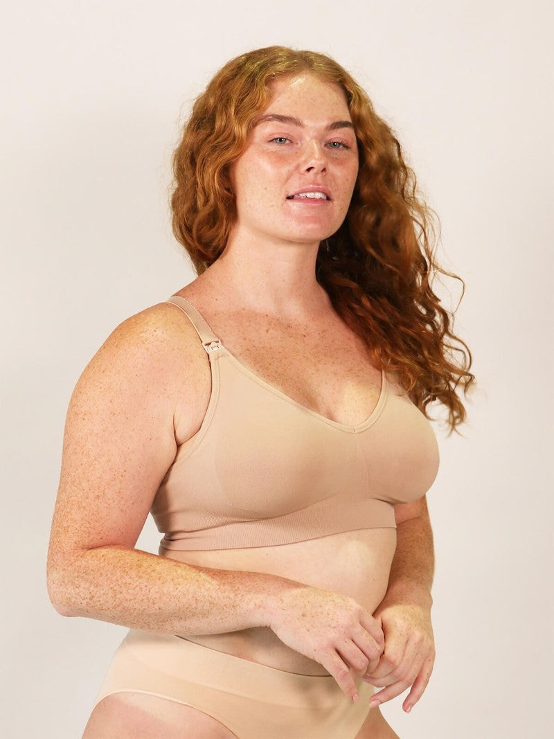 Woman wearing a beige nursing bra against a plain background