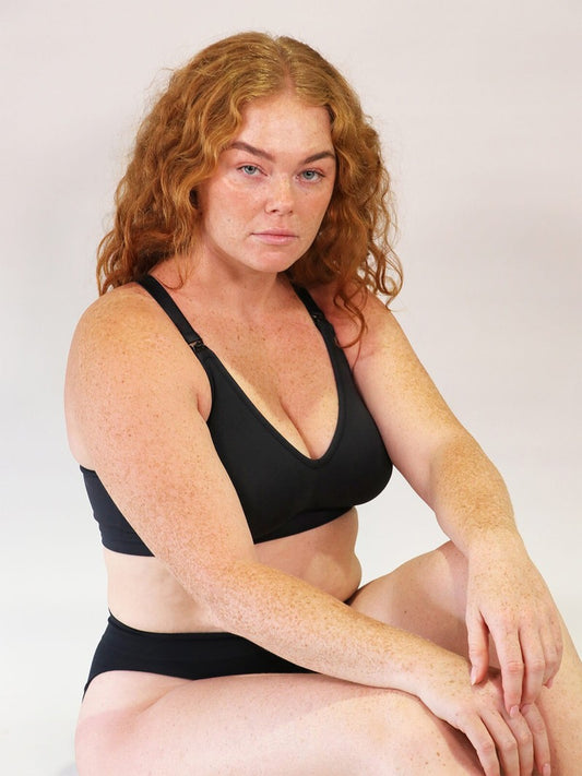 Woman wearing a black bra and underwear set against a plain background
