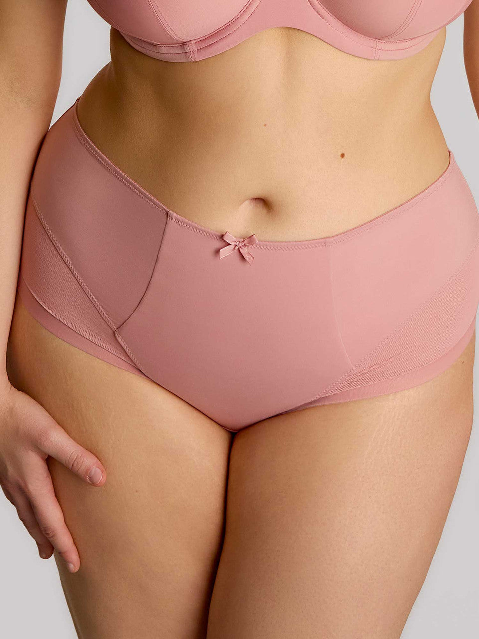 Person wearing pink high-waisted underwear and bra set on a plain background
