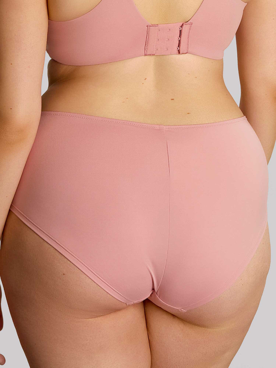 Person wearing a pink bra and underwear set on a plain background