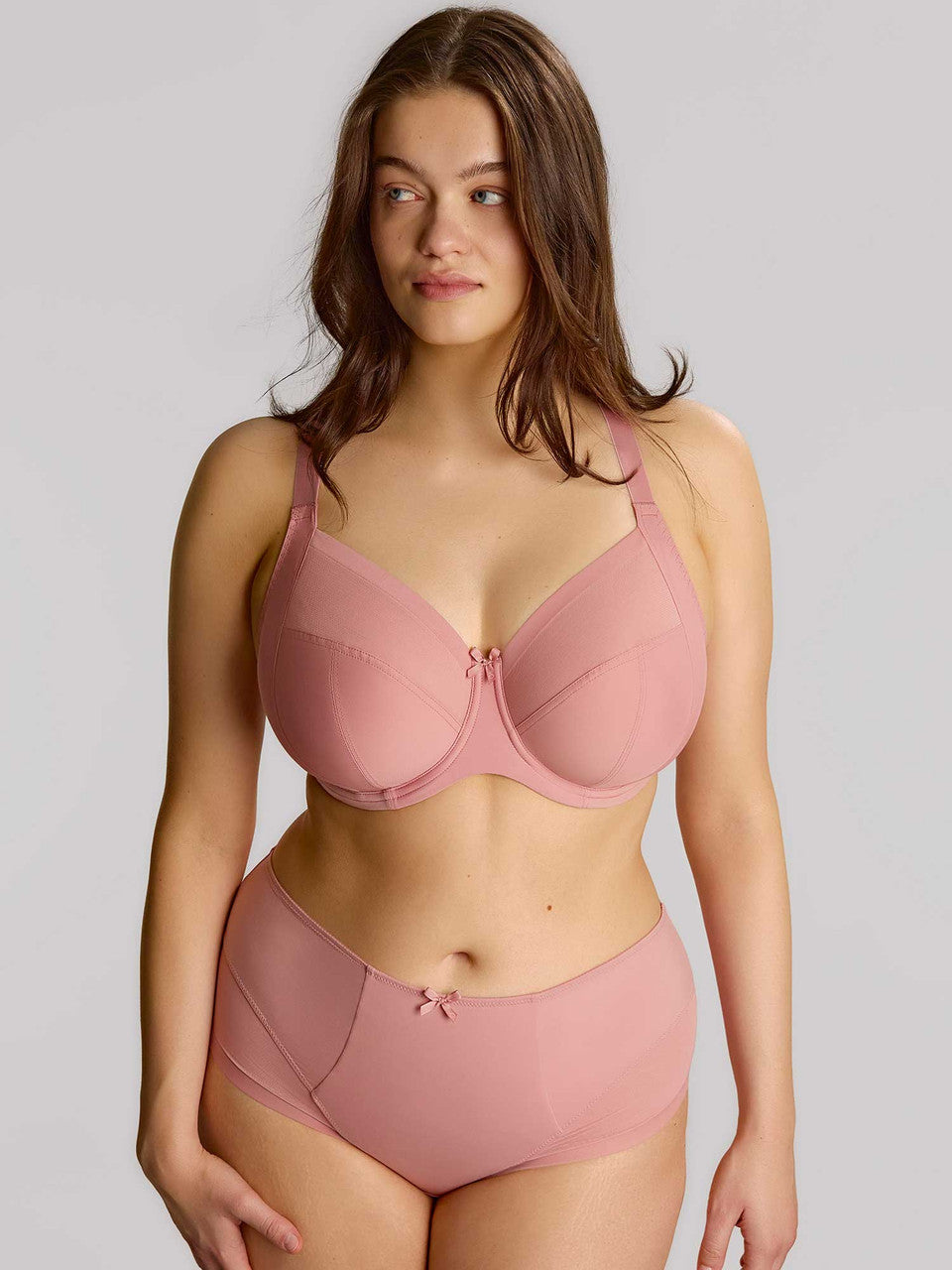Woman wearing a pink bra and underwear set against a plain background