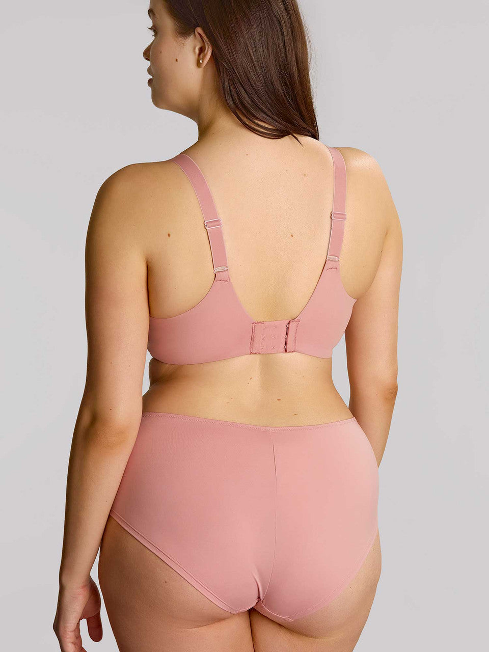 Woman wearing a pink bra and underwear set on a plain background