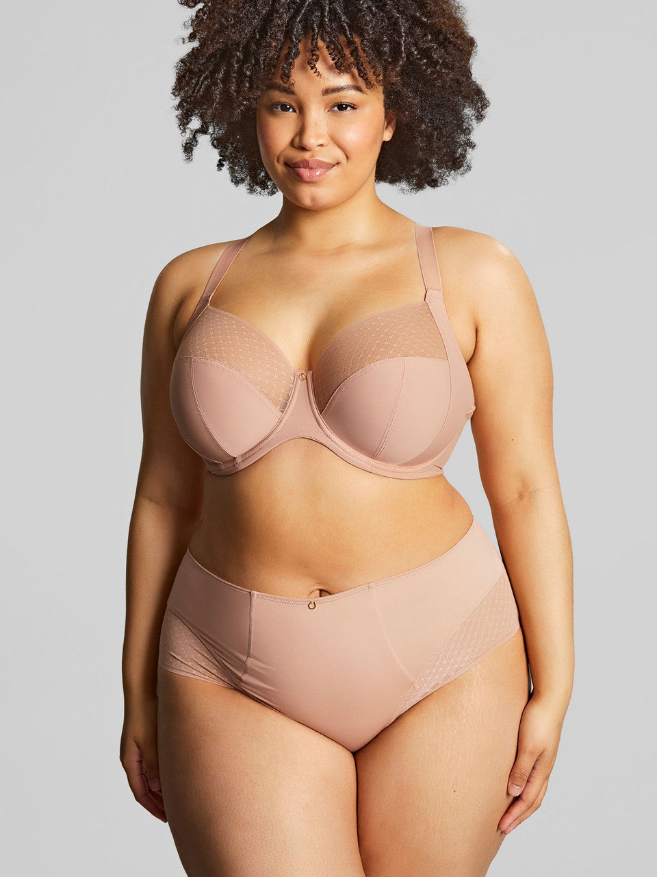 Woman wearing a beige bra and panties set against a plain background