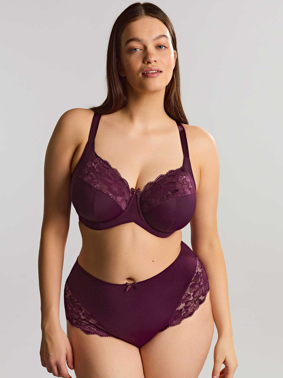 A woman modeling a deep plum bra and panty photographed against a gray studio background.