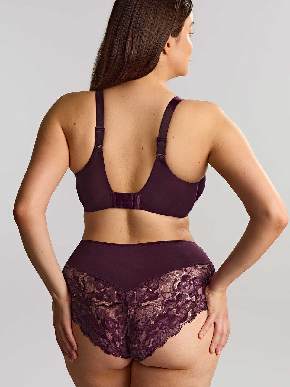A woman shown from the back wearing a matching lingerie set in deep plum against a gray background.