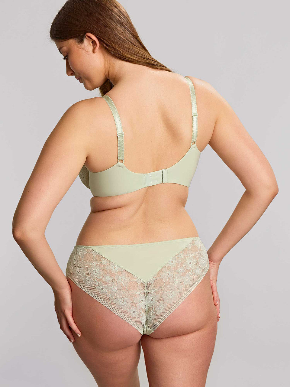 Woman wearing a light green bra and panties set on a plain background