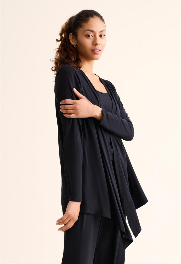 Woman wearing a black outfit with a flowing top against a plain background