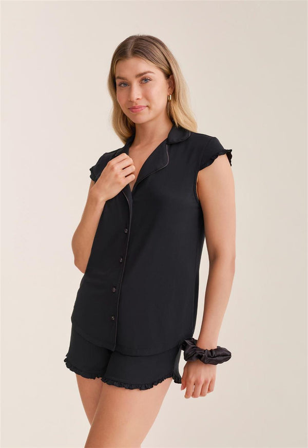 Woman wearing a black pajama shirt and shorts set on a beige background