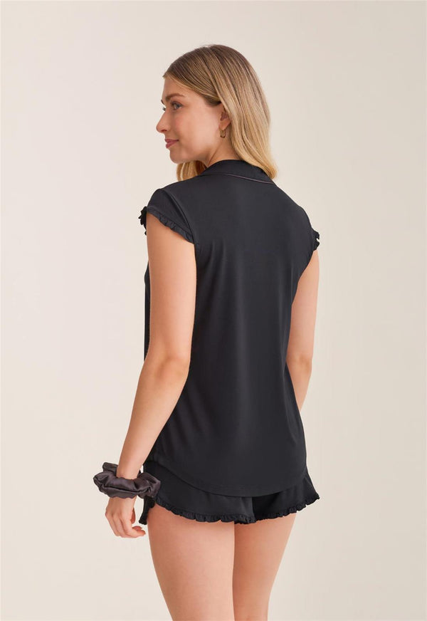 Woman wearing a black sleeveless pajama top and shorts on a beige background