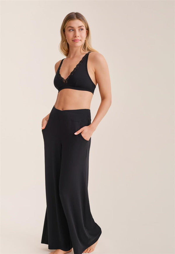 Woman wearing a black lace bralette and wide-leg pants on a beige background