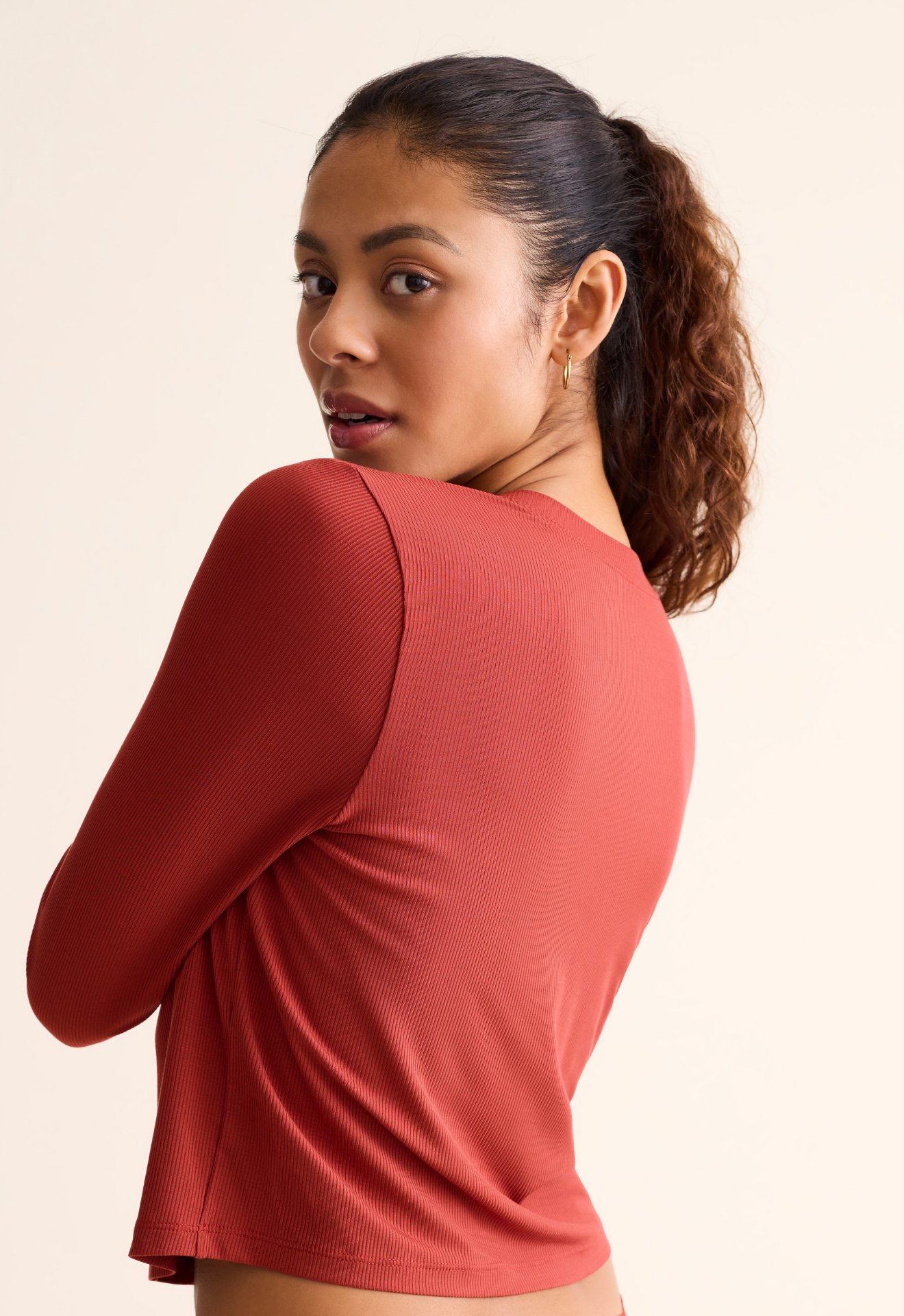 Woman wearing a red long-sleeve top against a beige background