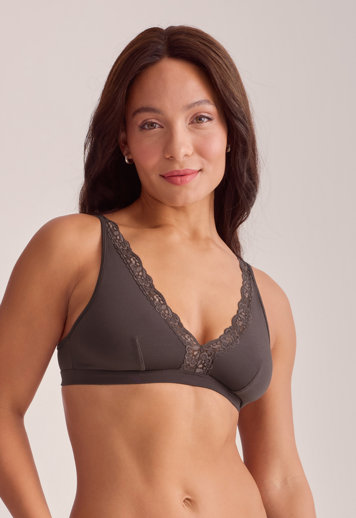 A woman modeling a brown wireless bra with black lace trim on a light gray studio background.