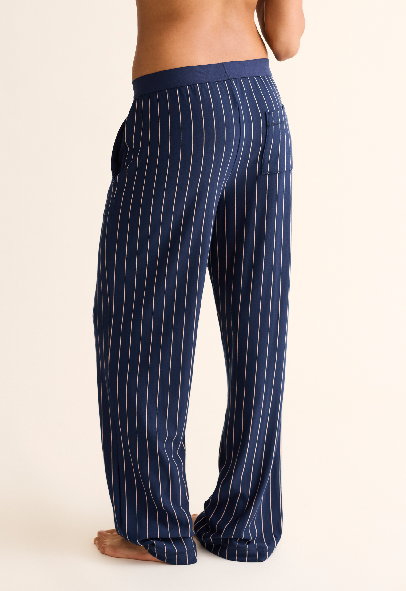 Navy pinstripe pajama pants worn by a person on a beige background