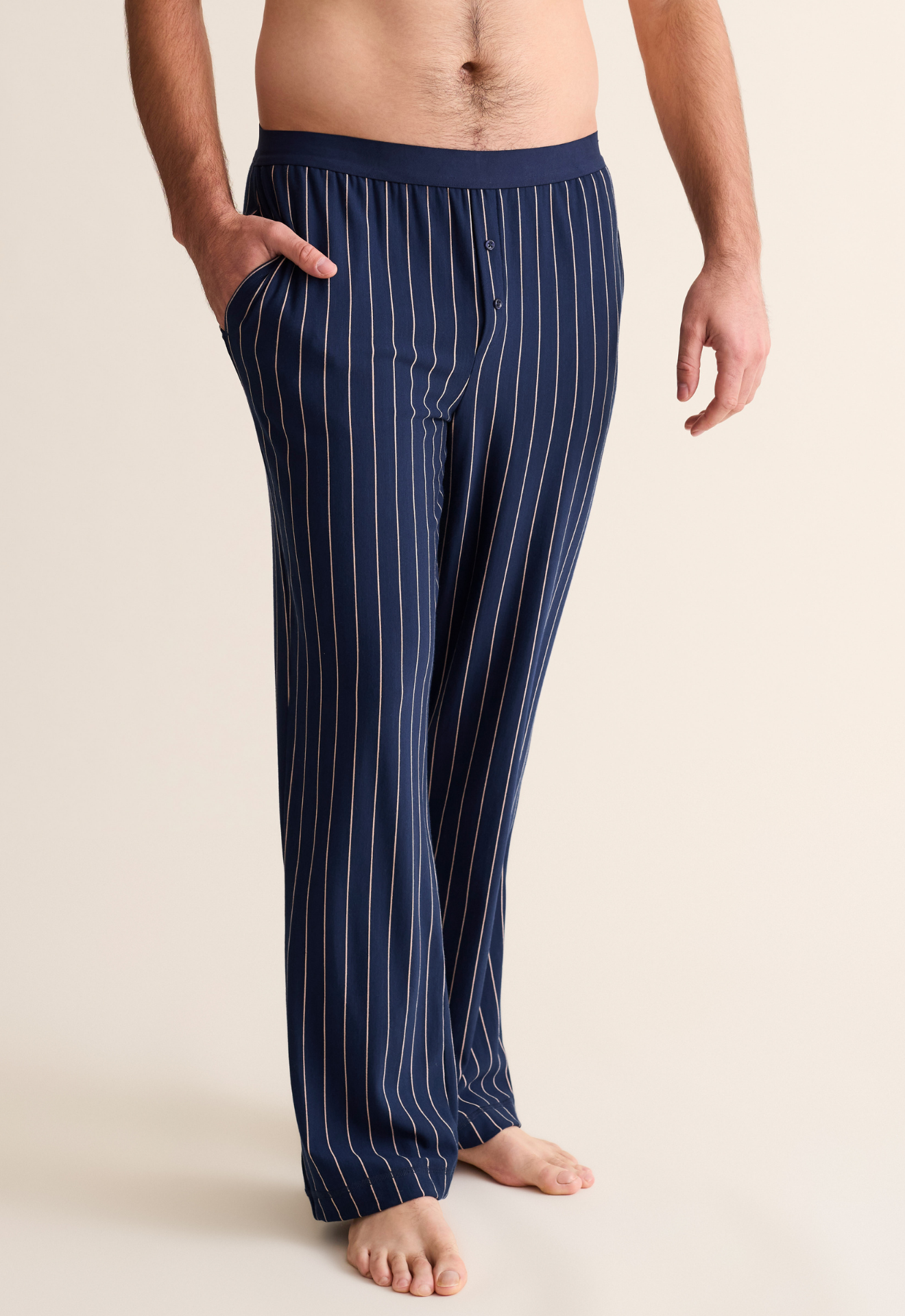 Navy pinstripe pajama pants worn by a person on a beige background