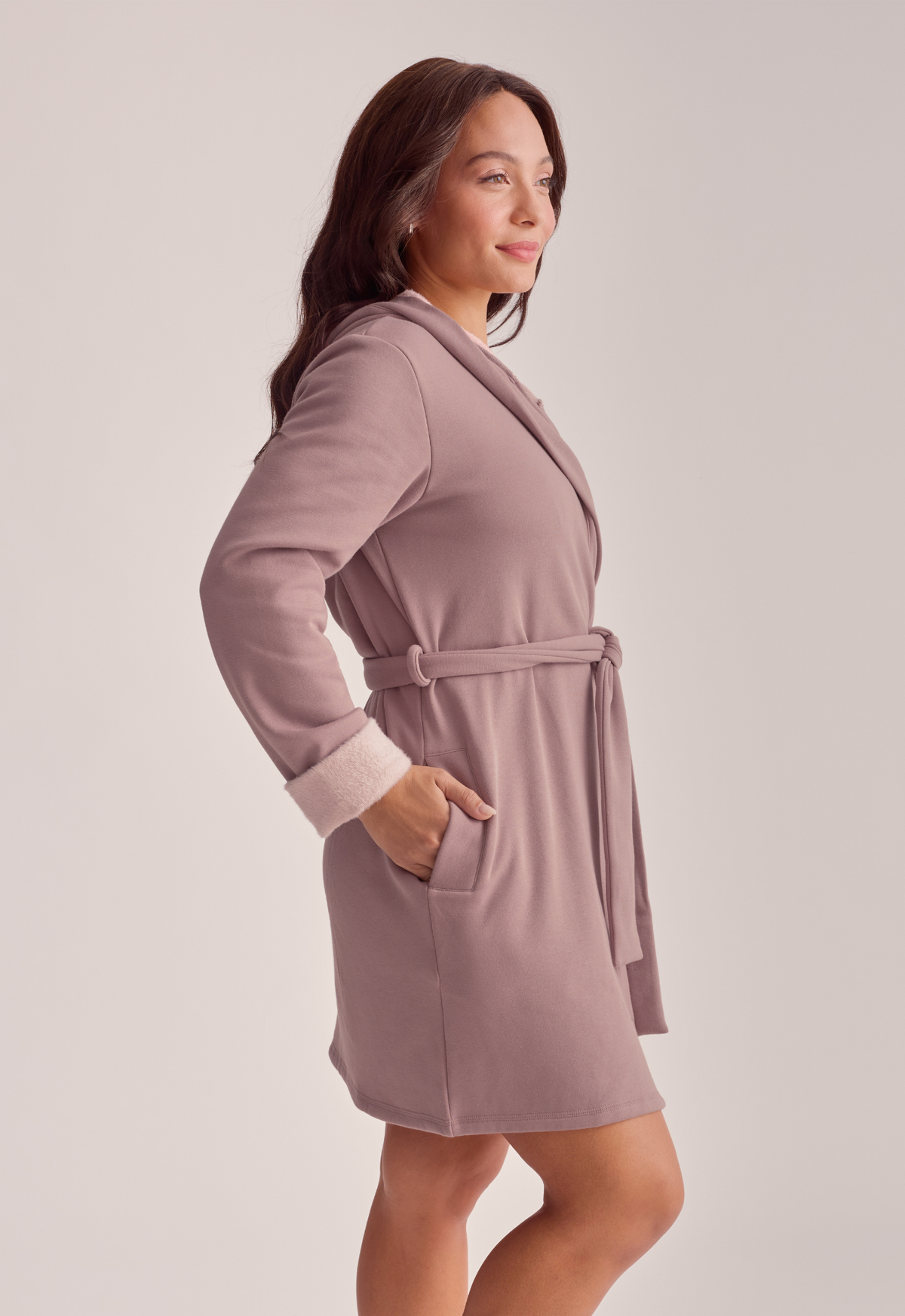 A woman wearing a mauve robe, shown in a side profile against a light gray studio background.