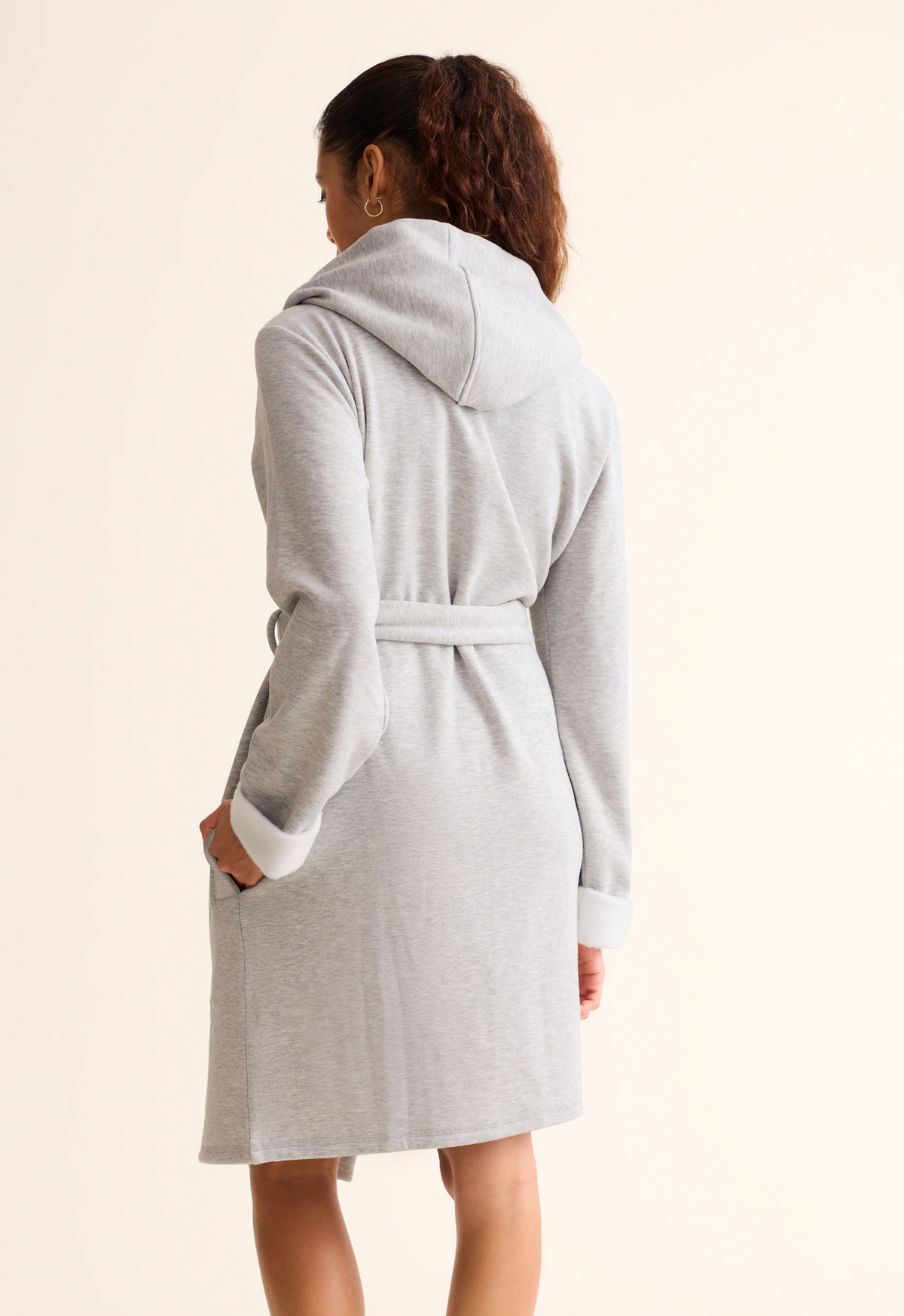 Person wearing a gray robe with a hood on a beige background