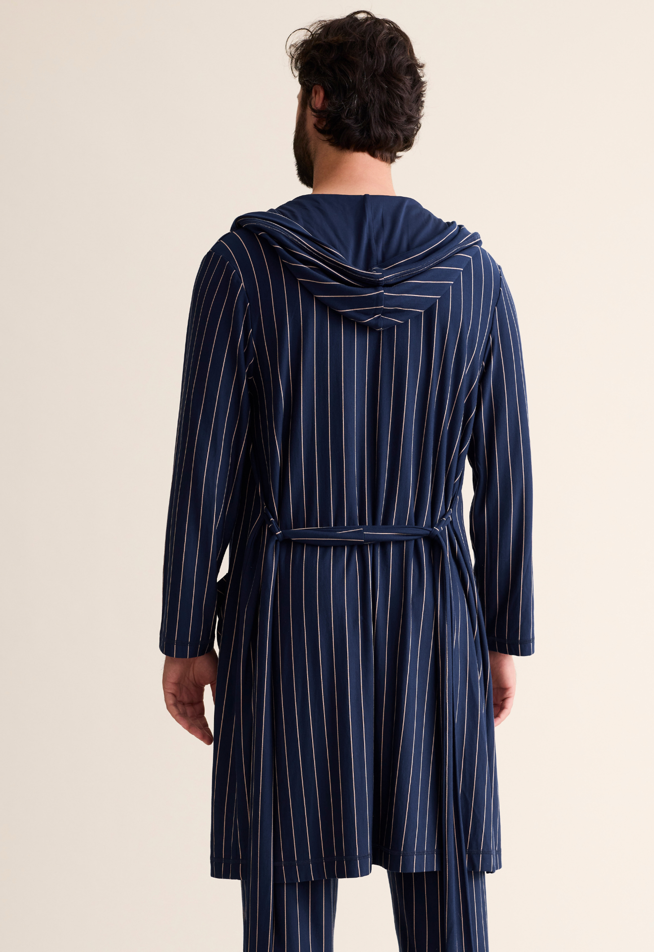 Person wearing a blue striped robe from behind on a beige background
