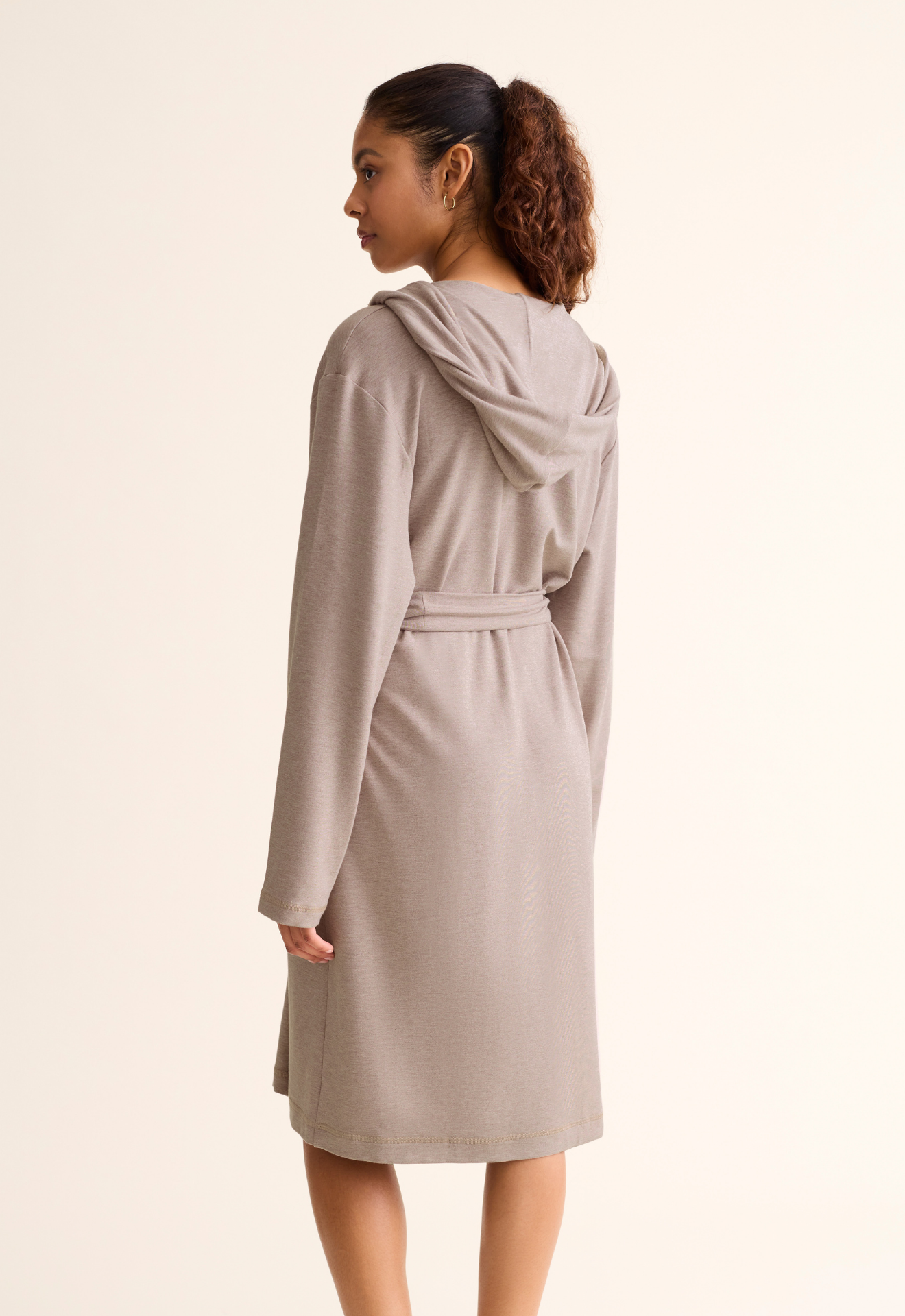 Woman wearing a beige robe with a hood on a plain background