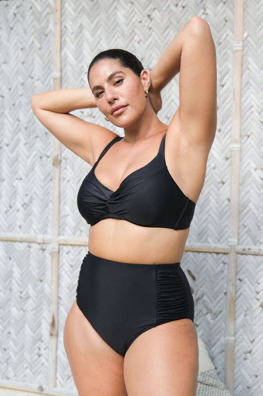 Woman wearing a black bikini against a textured wall.