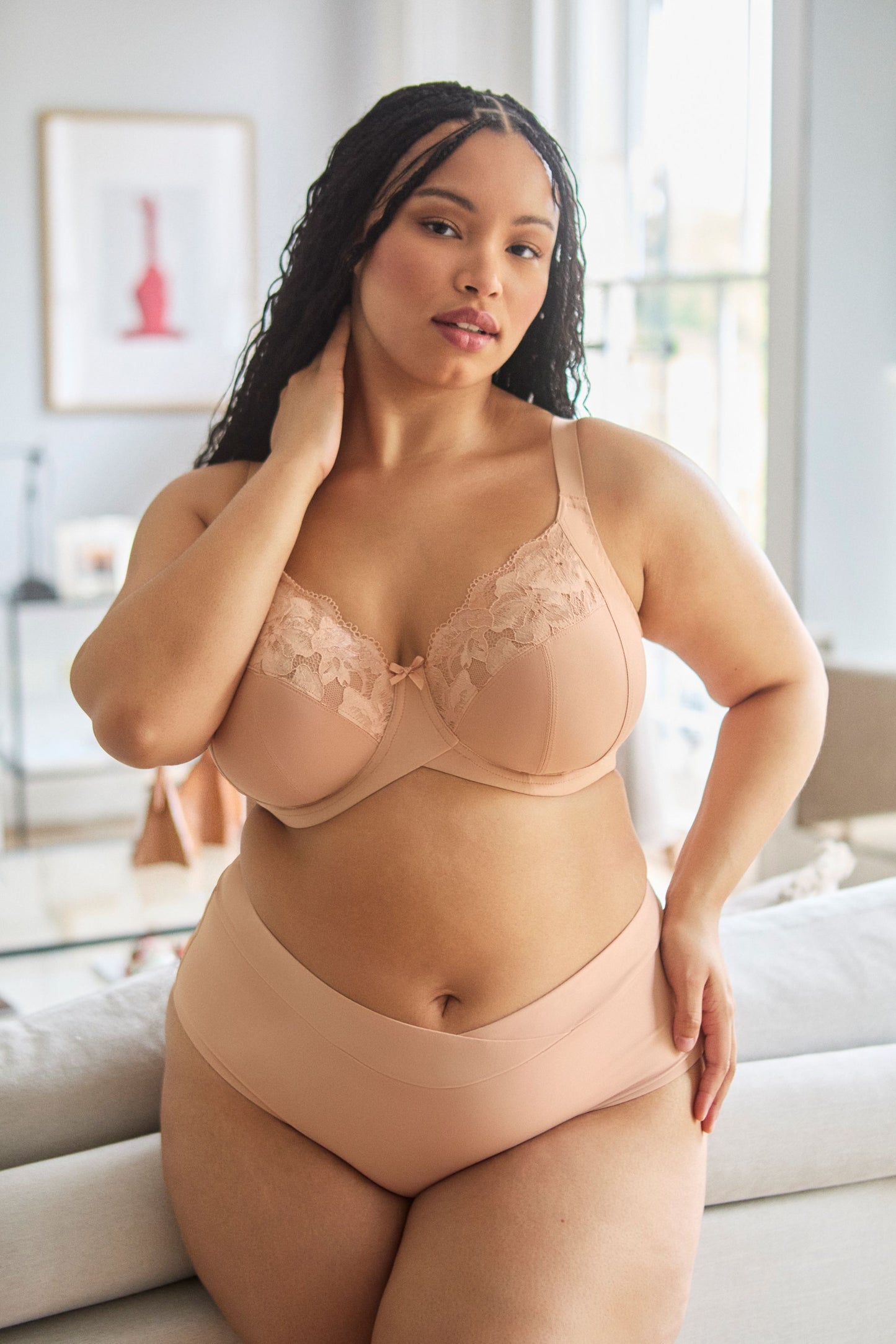 Woman wearing a beige bra and panties set in a bright room.