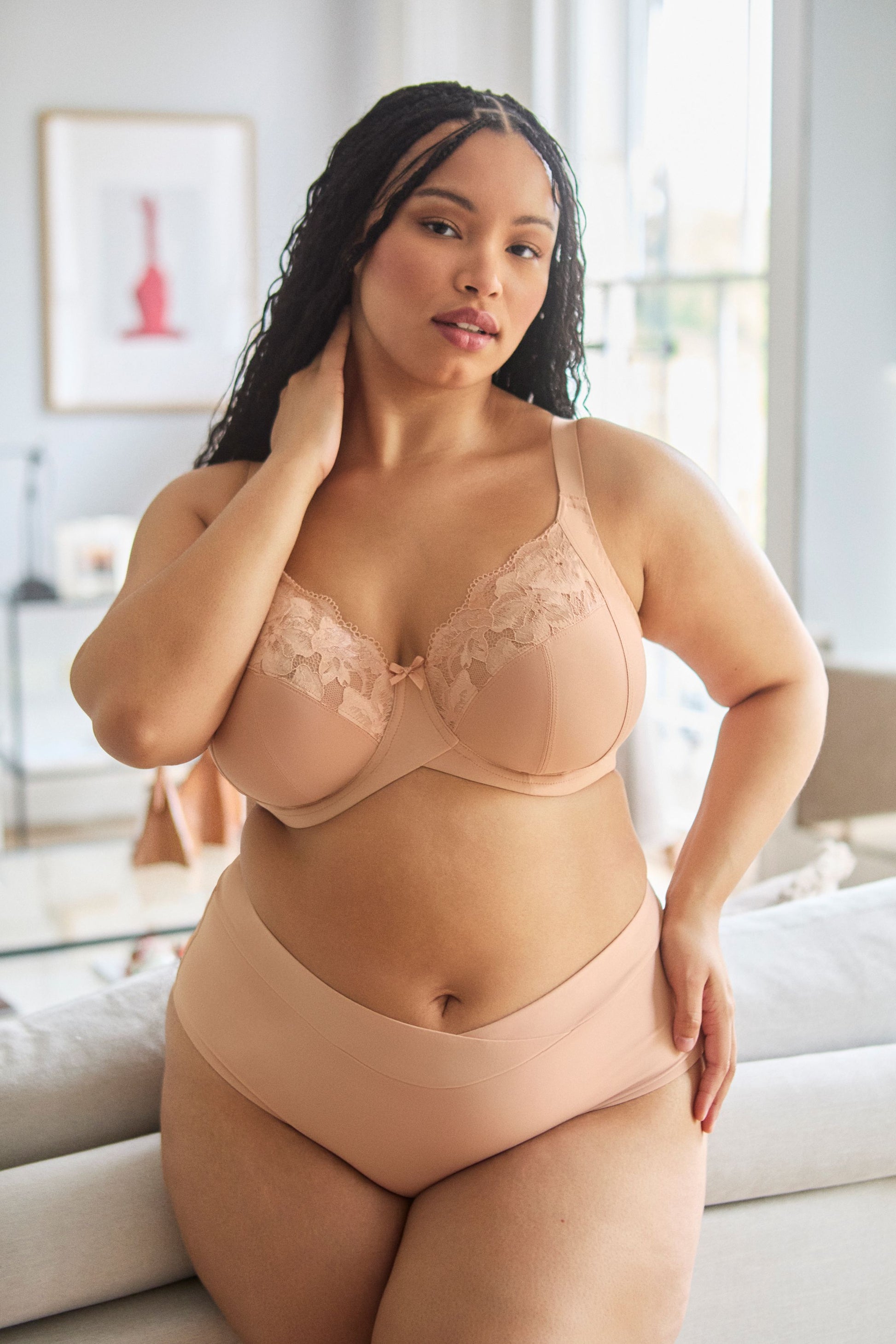 Woman wearing a beige bra and panties set in a bright room.