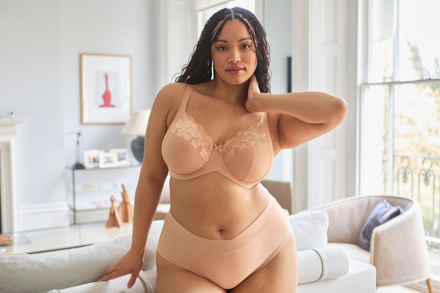 Woman wearing a beige lingerie set in a bright living room.