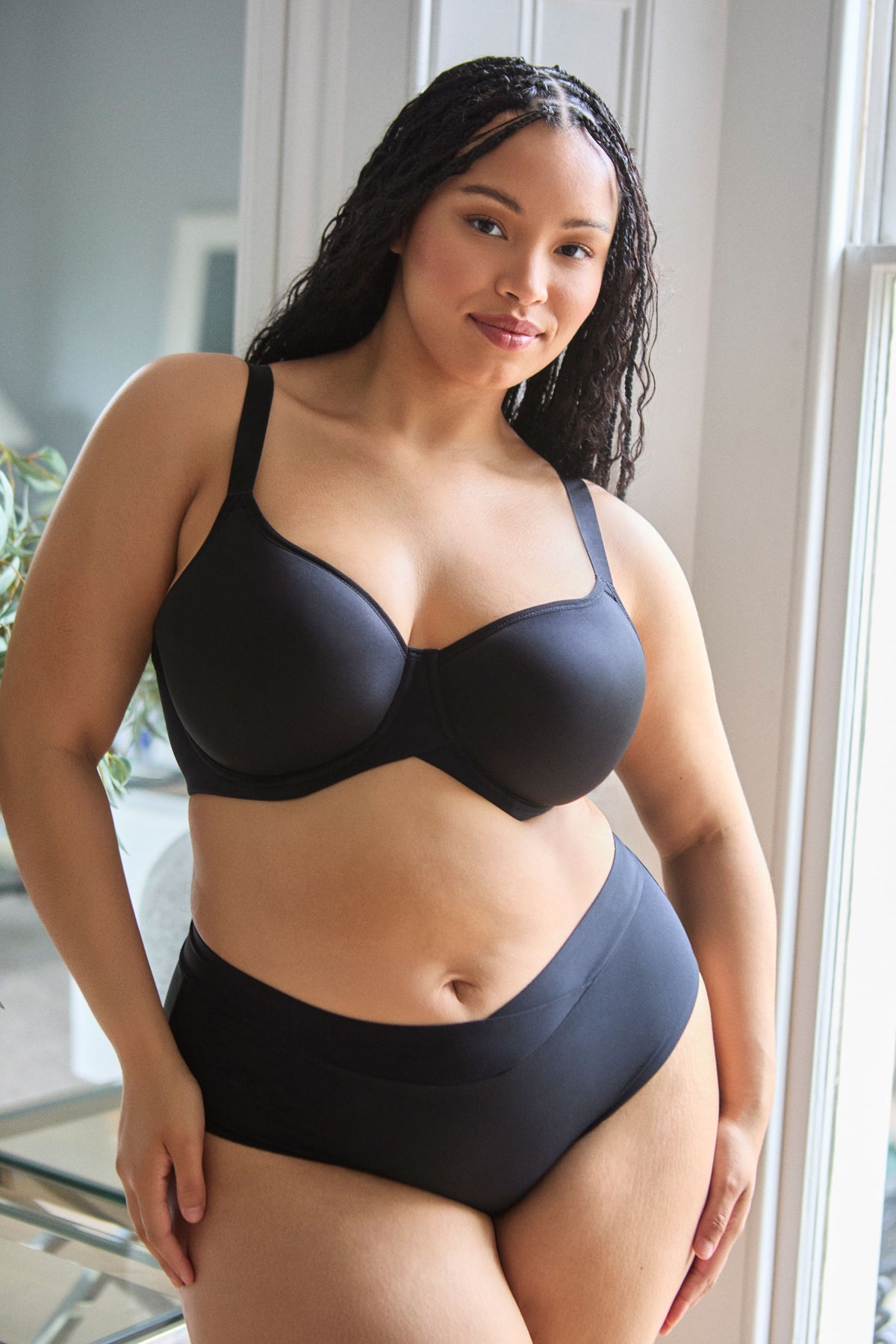 Woman wearing a black bra and high-waisted underwear in a well-lit room.