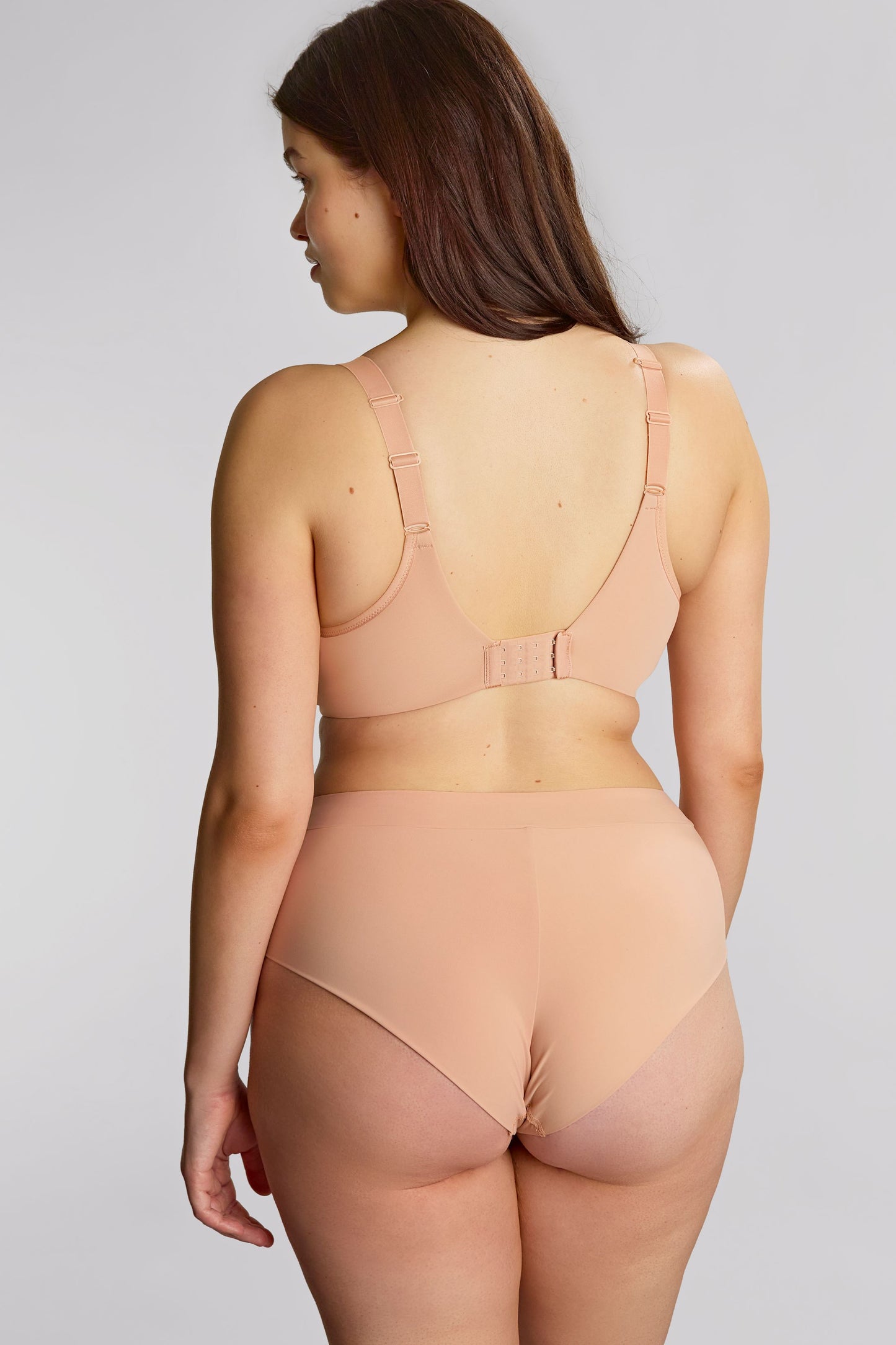Woman wearing a beige lingerie set against a plain background