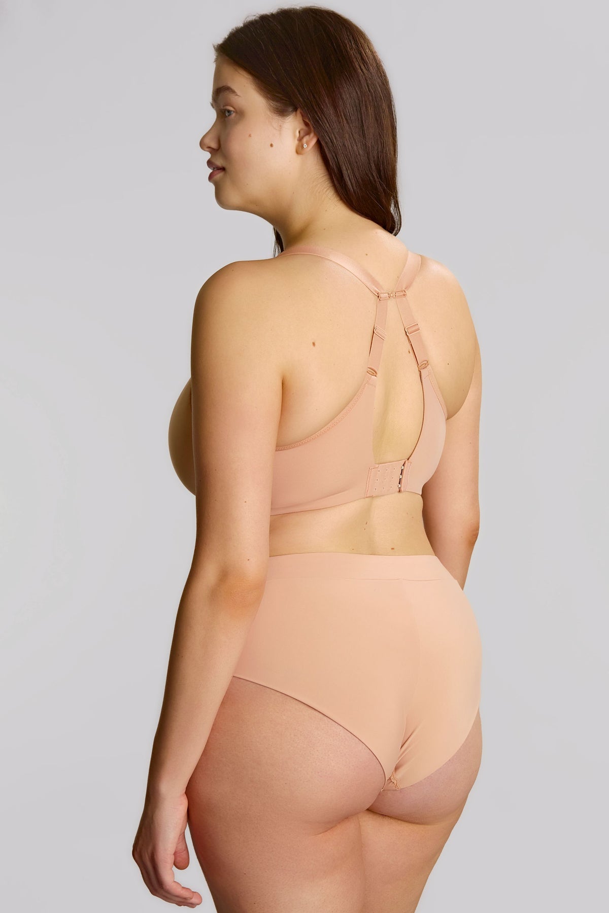 Woman wearing a beige bra and panties against a plain background