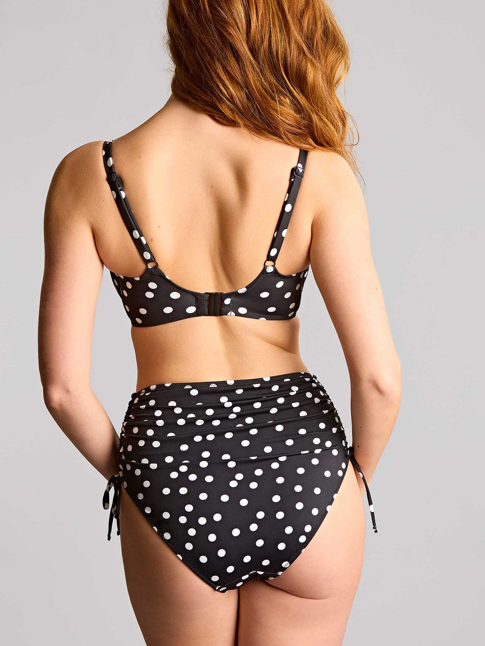 Woman wearing a black and white polka dot bikini against a gray background