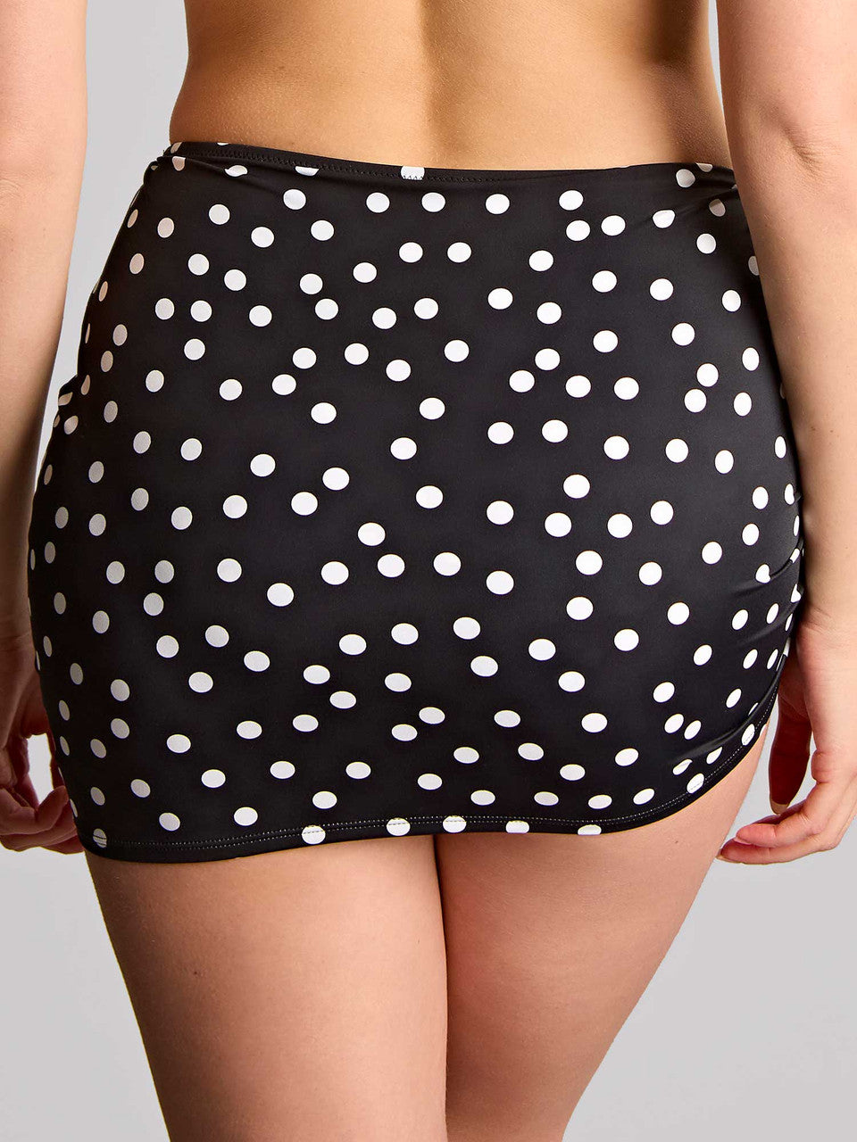 Back view of a black polka dot skirted swim brief worn by a person on a gray background