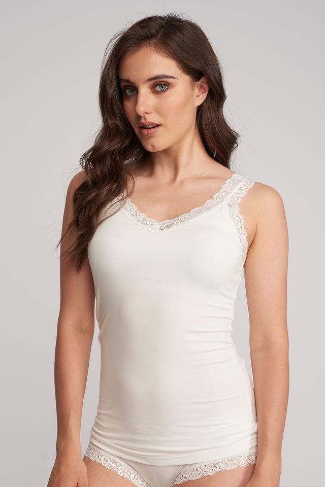 Woman wearing a white sleeveless top with lace trim on a plain background