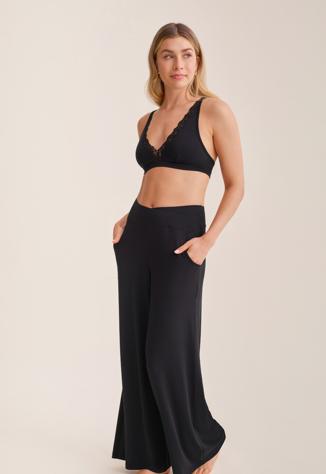 Woman wearing a black lace bralette and high-waisted black pants on a beige background