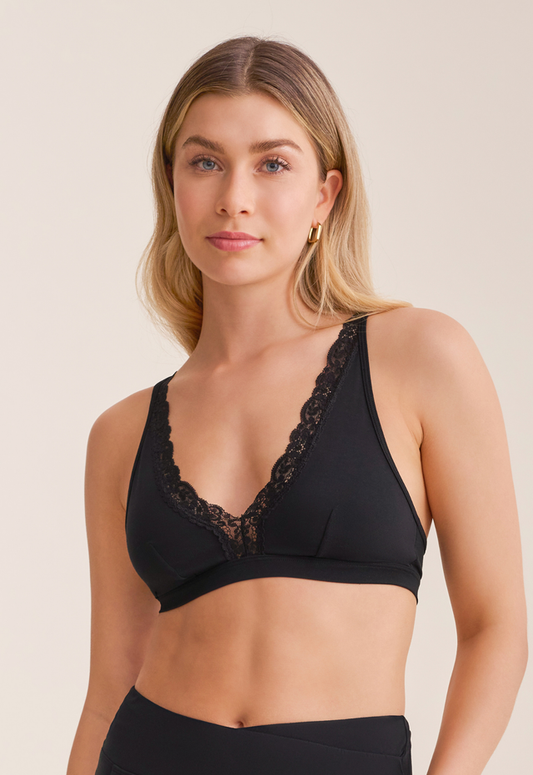 Woman wearing a black lace-trimmed bralette against a beige background