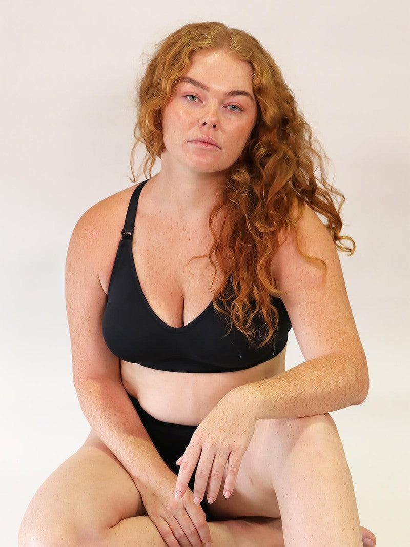 Woman wearing a black nursing bra sitting against a plain background