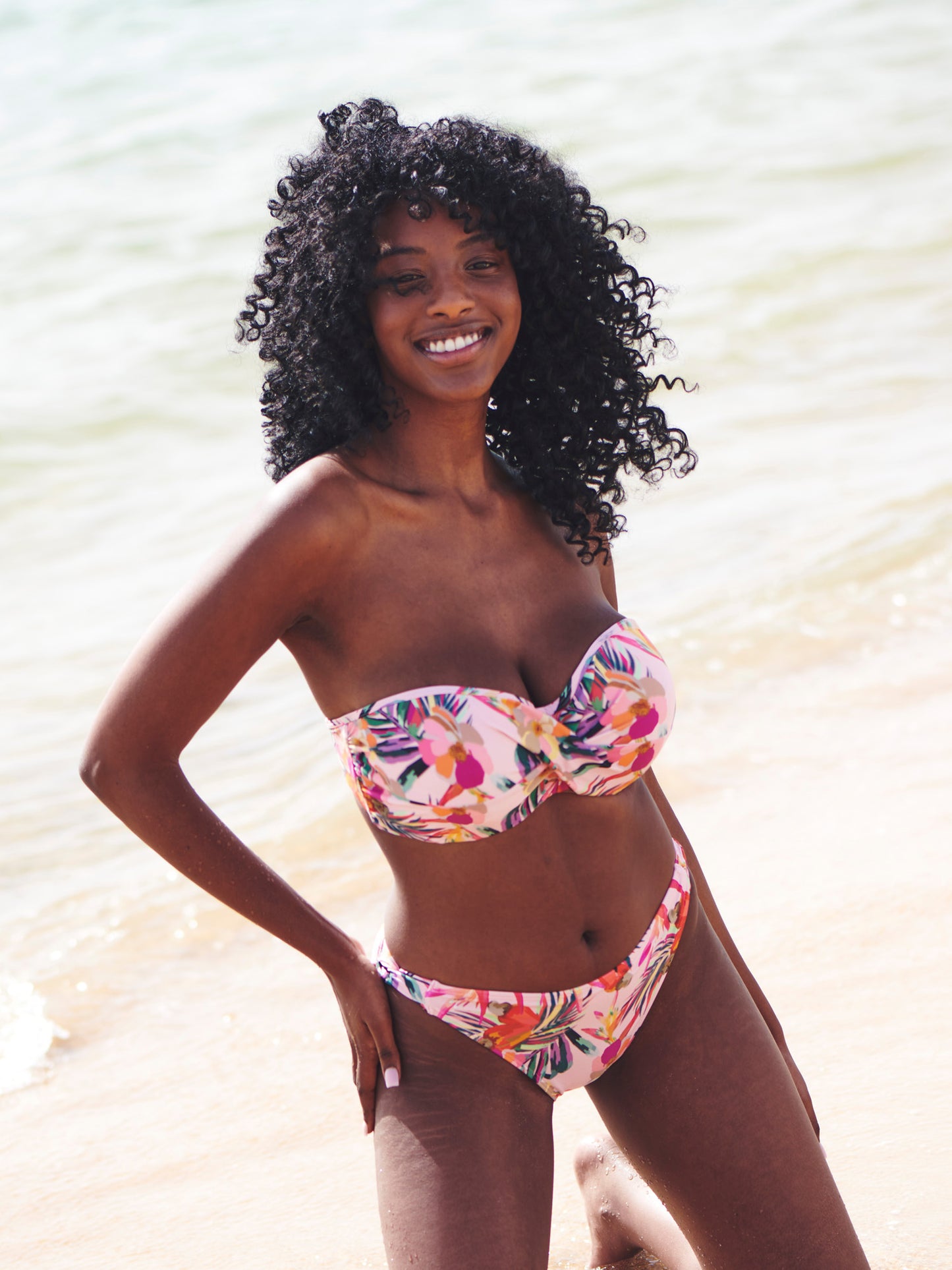 Model wears Paradise Twist Bandeau Bikini with Classic Pant in Pink Tropical Print. Lifestyle photo.
